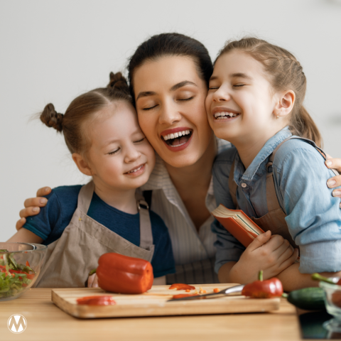 A mom smiles while hugging her two young daughters