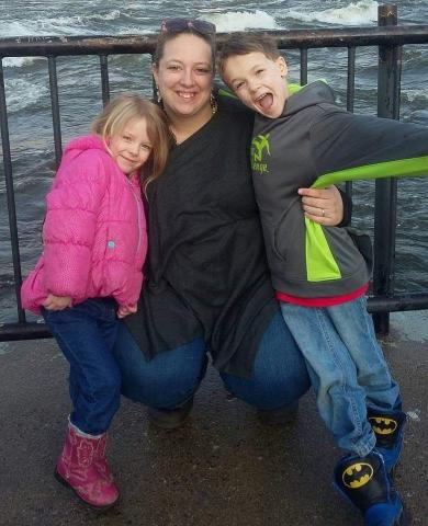 [IMAGE DESCRIPTION: A photo of a woman crouching and smiling at the camera, with two children on either side of her.]