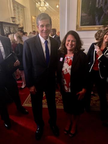 [IMAGE DESCRIPTION: MC Governor Roy Cooper stands with MomsRising NC Director Beth Messersmith, smiling at the camera after signing a paid leave bill.]