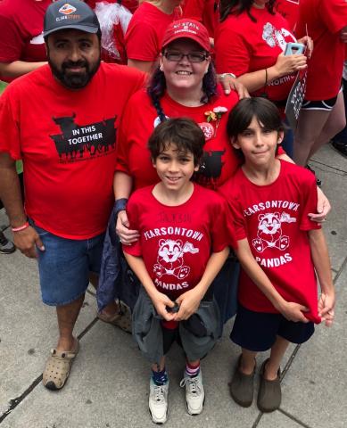 [IMAGE DESCRIPTION: A family of two adults, one with a beard, and two children, both with short dark hair, all wearing red shirts and smiles.]