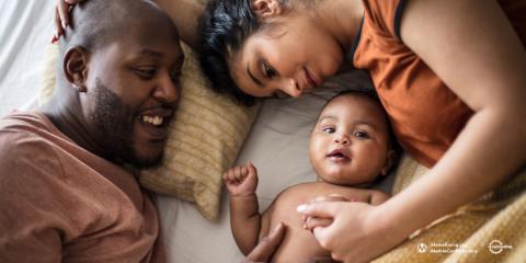 photo of a mother and father laying on a bed with a young baby