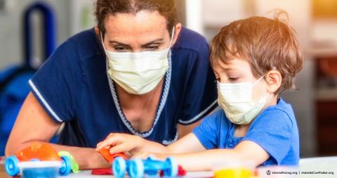 Woman sitting at a table with a child playing wit a building toy.