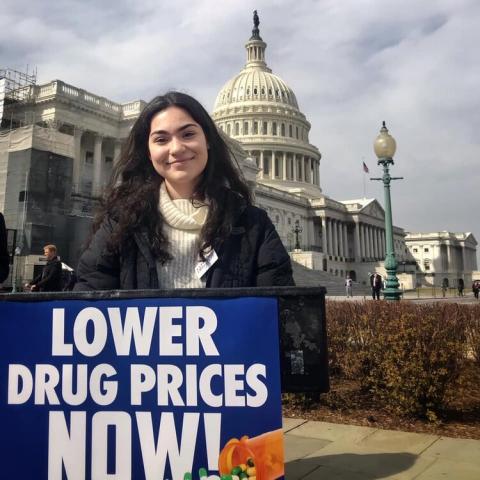 [IMAGE DESCRIPTION: A photo of a young woman with dark brown hair standing behind a poddium outside the US Capitol and smiling at the camera.]