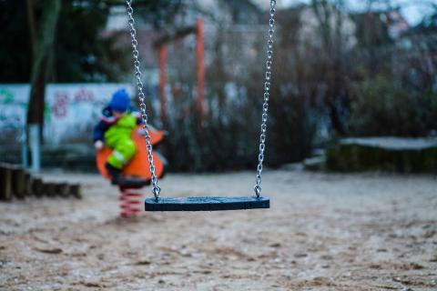 [IMAGE DESCRIPTION: A photo of an empty swing, with a child out of focus behind it.]