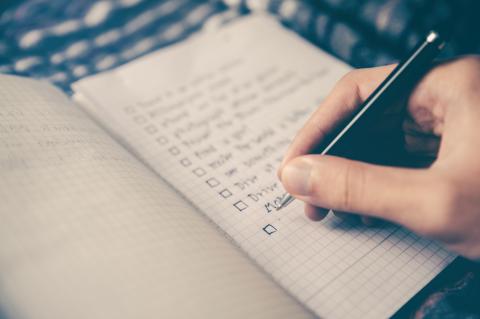 Hand holding pen, writing list on notepad.