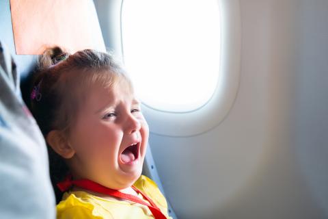 [IMAGE DESCRIPTION: A photo of a young child with blond hair in a half ponytail crying in an airplane seat.]
