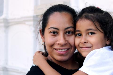 Woman holding daughter, smiling and looking at the camera