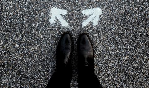 Black and white image shows 2 feet on the ground with 2 arrow in front of them pointing in different directions.