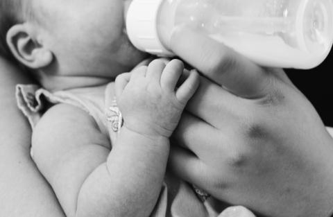 Baby held by a caregiver, being fed from a baby bottle 