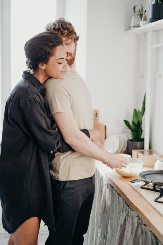Woman embraces her husband as he makes her pancakes for breakfast. Love is in the air.