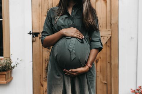 [IMAGE DESCRIPTION: A photo of a person with a pregnant belly in a green dress standing in front of a wooden door.]