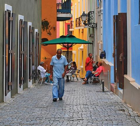 [IMAGE DESCRIPTION: Man walks down an alley surrounded by colorful buildings in Puerto Rico.]