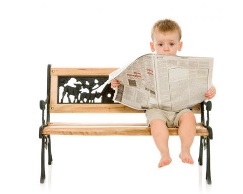 toddler boy sitting on a bench reading a newspaper