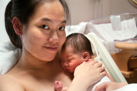 A mom with brown eyes and black hair hold her newborn baby