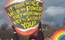 Two people at the No Kings march hold a mouth-shaped sign with an RBG quote and a rainbow fan.