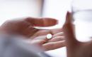 Close up of a hand holding a white mifepristone pill (labeled 'M') with a glass of water nearby. 