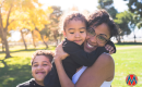 A mom with brown skin holds her toddler while her young son hugs her