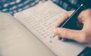 Hand holding pen, writing list on notepad.