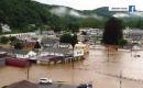 A photo showing a small town submerged in muddy water with a wooded mountain in the background
