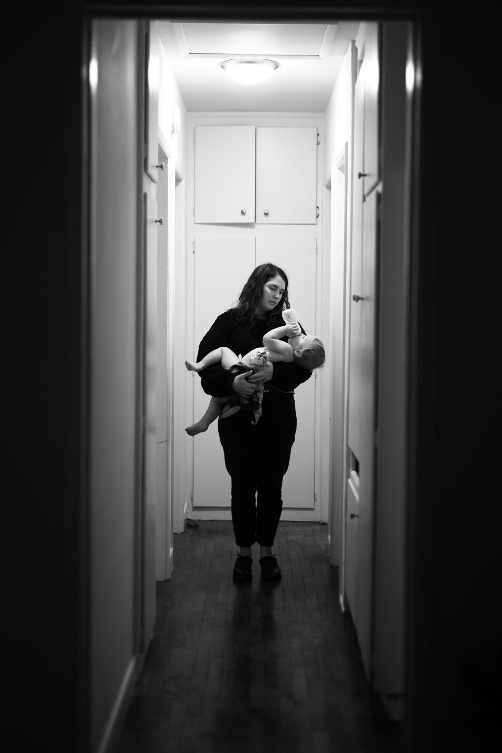 Woman in dark hallway holding toddler drinking from a bottle. 