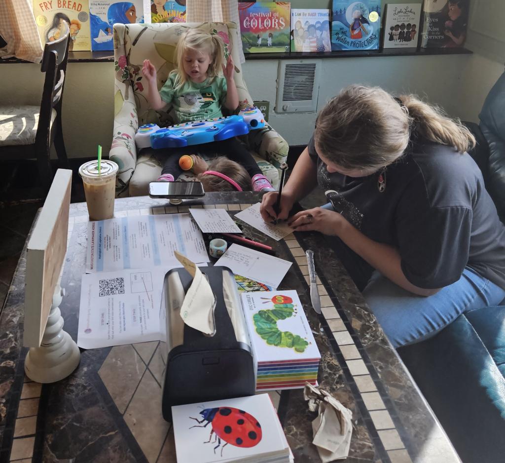 MomsRising Washington volunteer Isabelle writing postcards with her daughter