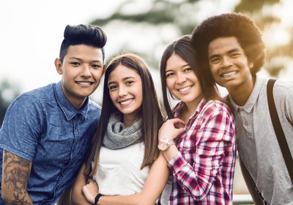 A group of teenagers of various ethnicities and genders smiles at the camera
