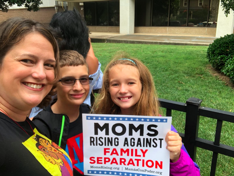 An adult and two children at a rally, holding a sign that says "Moms Rising Against Family Separation"