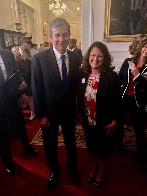 [IMAGE DESCRIPTION: MC Governor Roy Cooper stands with MomsRising NC Director Beth Messersmith, smiling at the camera after signing a paid leave bill.]