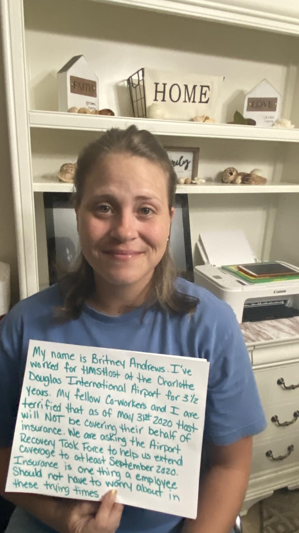 [IMAGE DESCRIPTION: A photo of a woman wearing a light blue tshirt and holding a sign.]