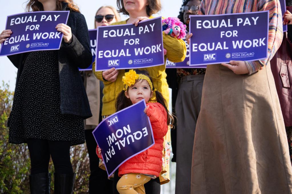My daughter, gazing off into the distance, holding a sign demanding "Equal Pay Now" upside down.