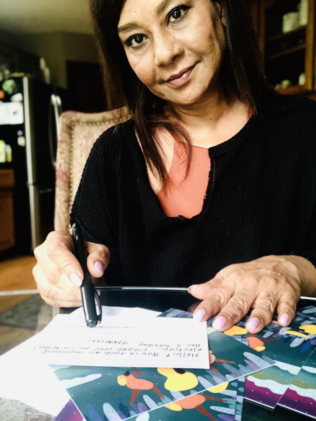 Photo of a MomsVote 2020 postcard volunteer filling out cards at her kitchen table