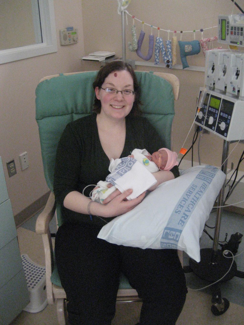 [Photo of Nicole holding her preemie baby in a chair at the hospital.]