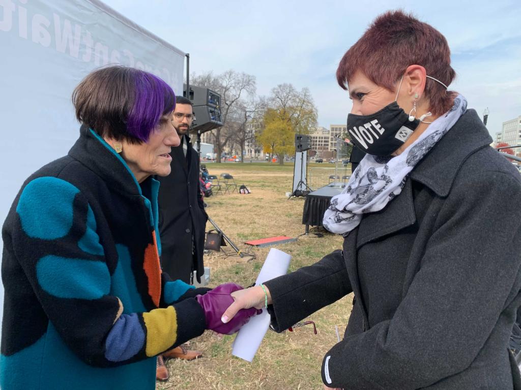 Two women facing each other, shaking hands. 