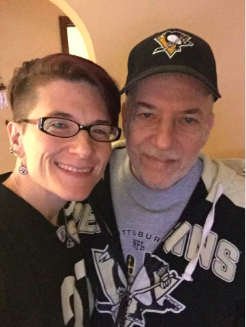 [IMAGE DESCRIPTION: An adult woman with short dark hair and her father, wearing a black baseball cap, look at the camera.]