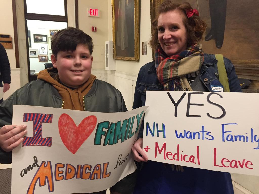 [IMAGE DESCRIPTION: Mother and son look at camera, smiling, holding sign for paid family and medical leave in New Hampshire.]
