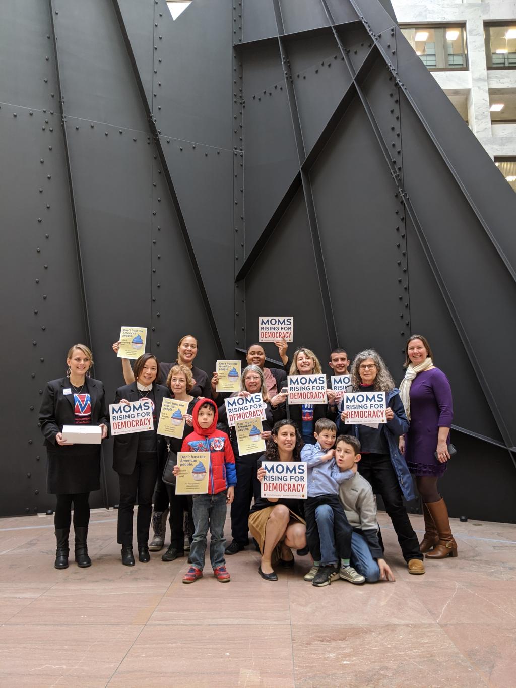 [IMAGE DESCRIPTION: A photo of MomsRising volunteers in front of the black modern mountain metal sculpture in the US Senate building.]