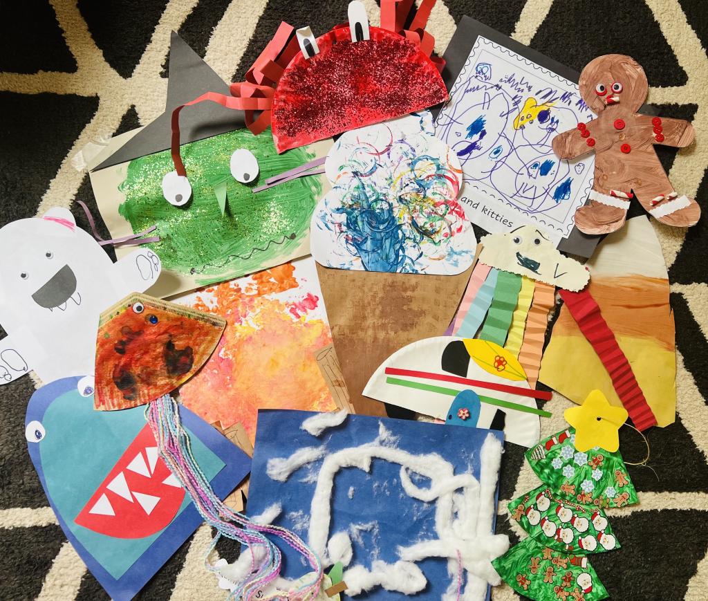 Childs work including a paper crab, cloud with rainbows hanging down, blue monster, blue paper with cotton ball clouds, Christmas tree, coffee filter jellyfish, green witch and other paintings and drawings.