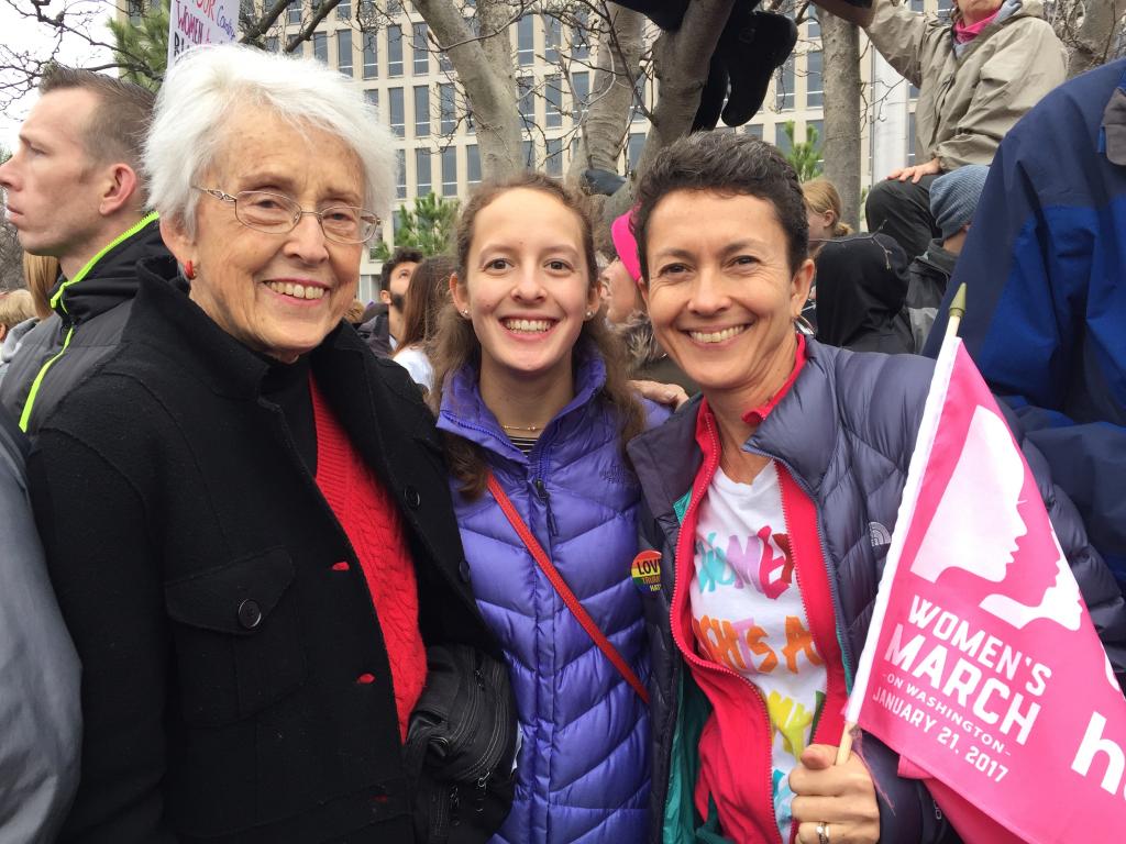 [IMAGE DESCRIPTION: A photo of three people smiling at the camera, one holding a pink flag.]