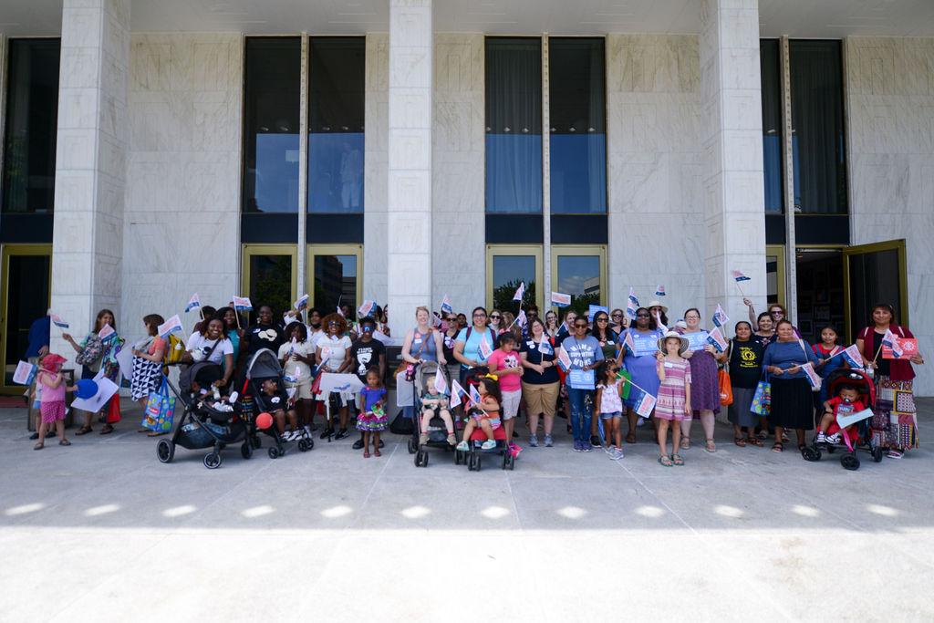 Group of mothers with their children, holding signs in front of the Raleigh General Assembly with their children.