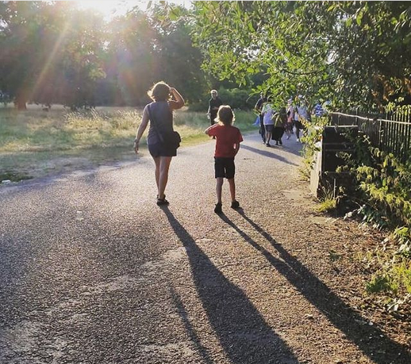 Mother and child walking away from the camera in a park with long shadows behind them