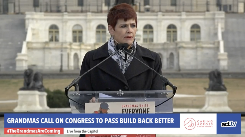 Woman at a podium with text on the lower third of screen that reads "Grandmas Unite!"