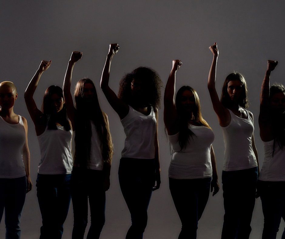 Variety of women standing side by side with their right fists raised in the air. 