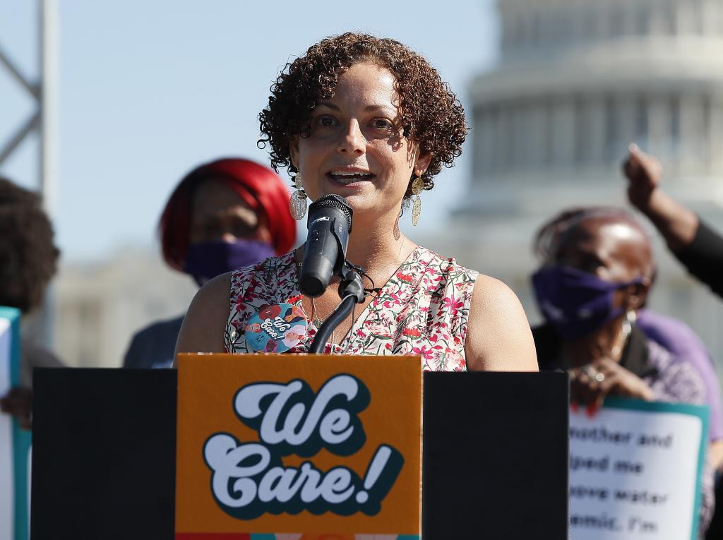 A woman speaking at a podium that has a sign that says "We Care"