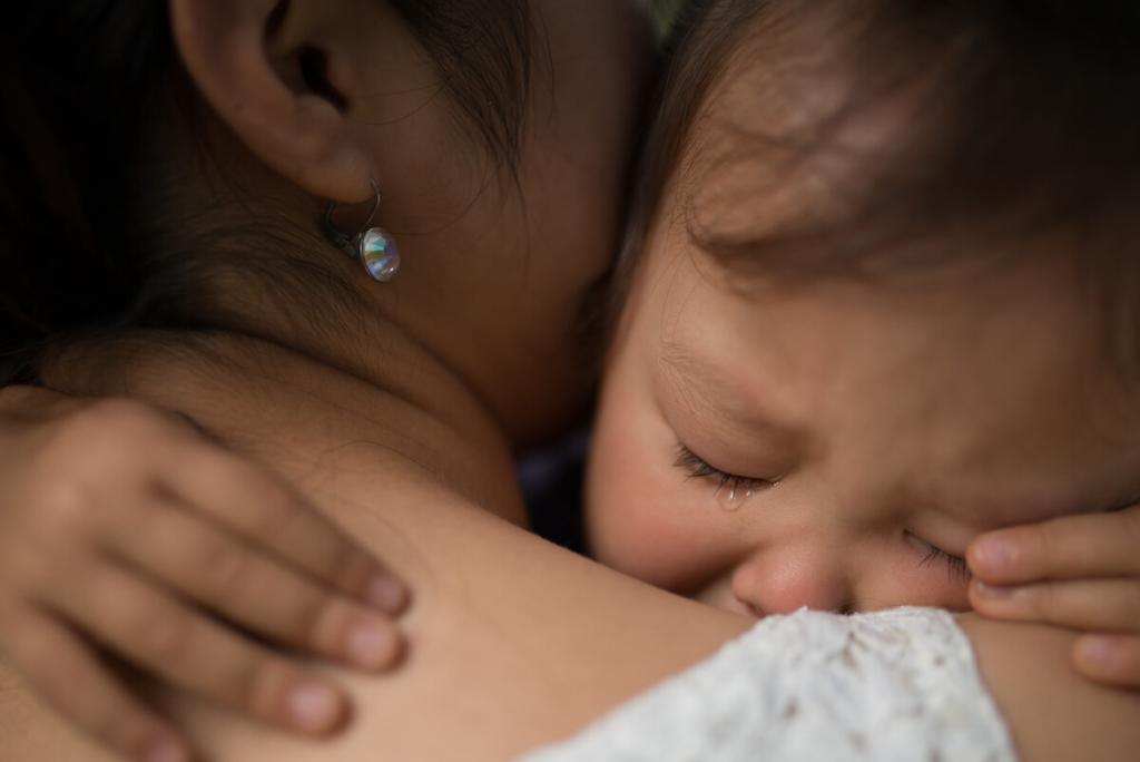 Young child hugging mother's neck with a tear on their cheek. 
