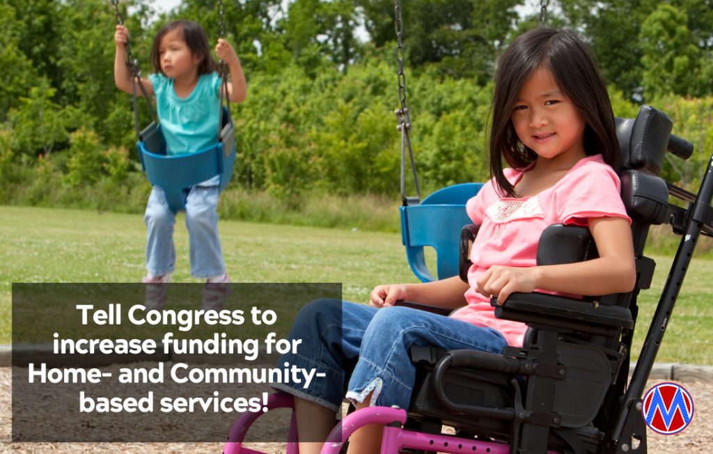 A girl with brown hair in a wheelchair sits smiling on a playground while her sibling swings