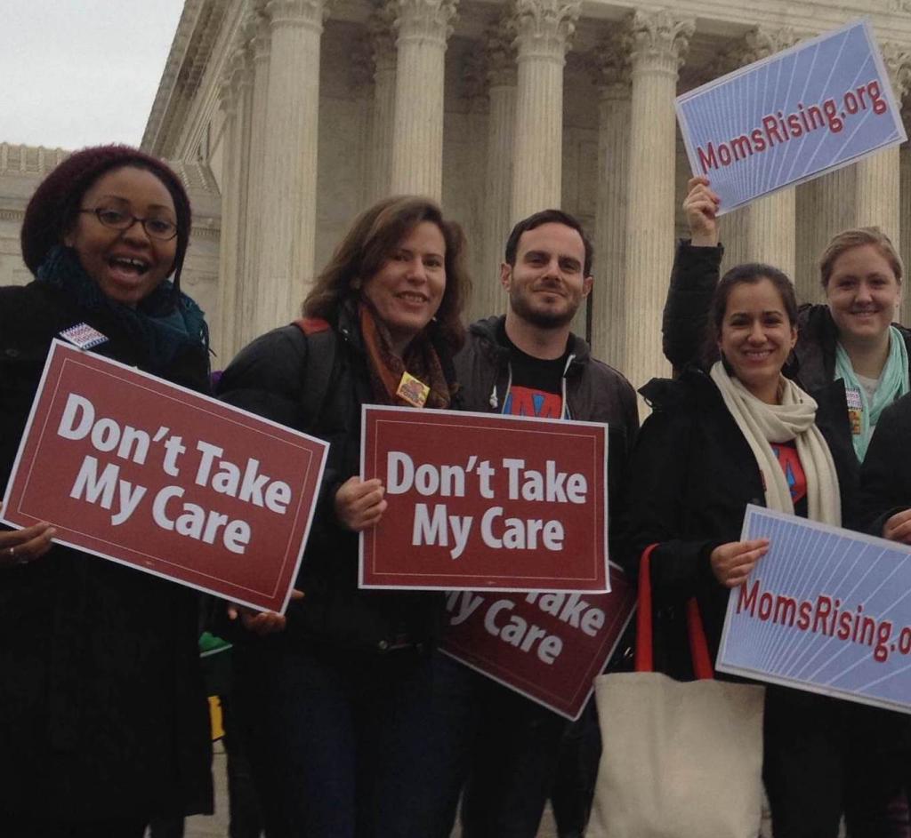 A diverse group of people hold "Don't Take My Care" signs in front of the Supreme Court Building