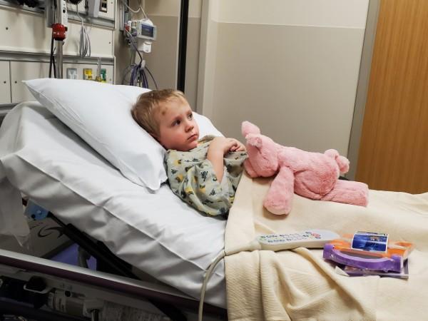 A young boy lays in a hospital bed holding a stuffed animal.
