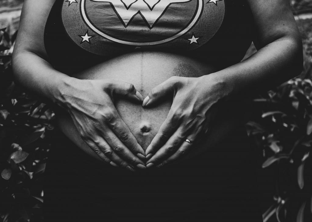 Photo of pregnant mother's belly, her hands forming a heart shape