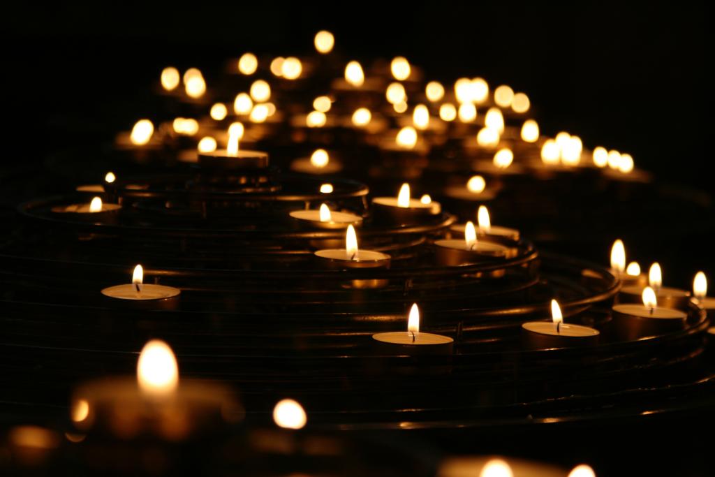 Many small candles lit up in a dark space. 