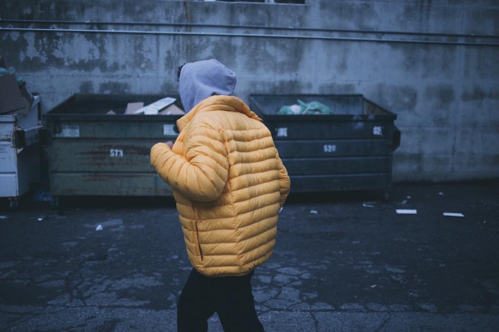 Photo by @RaffikLopes on Unsplash. Image Description: Person walking outside. In the background are several full garbage bins.